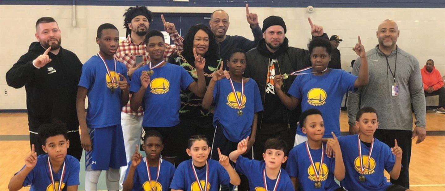 group photo of kids wearing medals and coaches, all holding up their index finger like the number one
